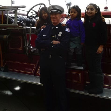 Three young girls stand behind a firefighter on an old fashioned fire truck